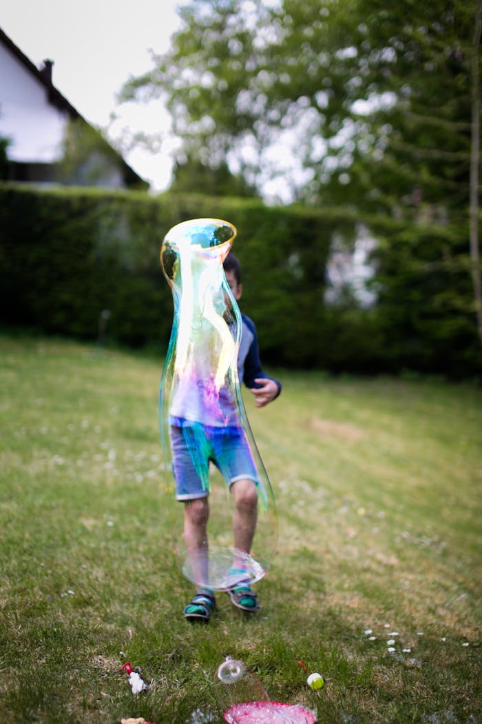 A child joyfully plays with a giant soap bubble in a grassy field.